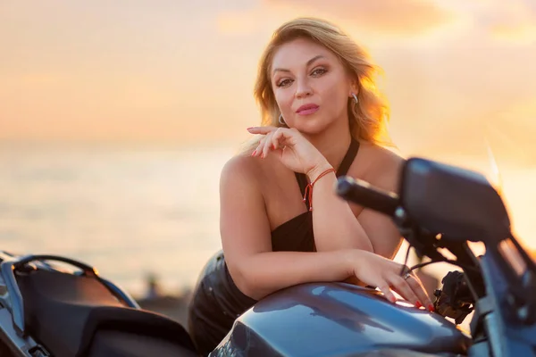 World motorcyclist day. Portrait of beautiful adult blonde woman confidently poses by a motorcycle. The concept of motorbike travel.