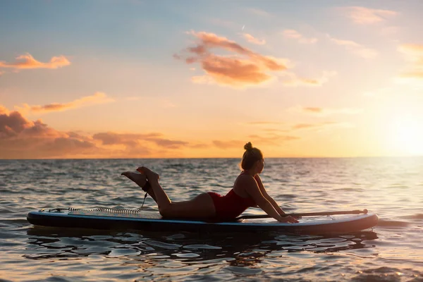 Silhouette of plus sized woman in bikini posing lying on a sup board. Copy space. Sunset sky on the background. The concept of water sports and summer vacation.