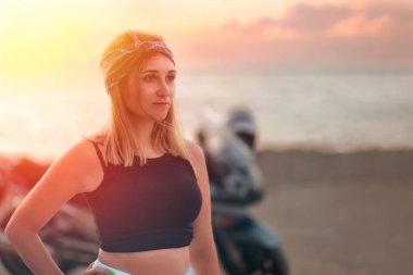 Freedom and travel. Portrait of young independent caucasian woman. Golden sunset and motorcycle in the background. The concept of the World Motorcyclist Day.