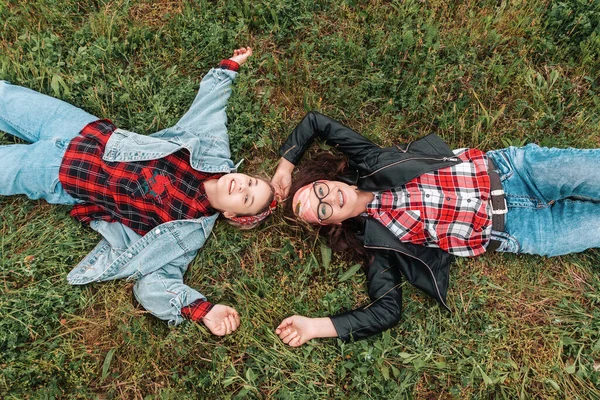 Portraits of happy Caucasian woman and teen girl are lying on their backs on the grass and looking at the sky. View from above. The concept of carefree, friendship and family psychology.
