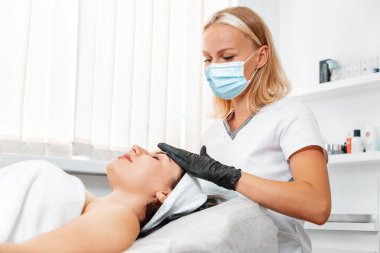 A cosmetologist in a medical mask massages a client in a beauty salon. The concept of rejuvenation and beauty treatments.