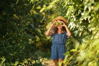 Funny little girl in a straw hat holds passion fruit near her eyes. Summer gardener. The concept of organic farming and harvesting.