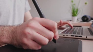 Man takes stylus from drawing tablet and begins to draw. Hand close-up. Side view. Concept of retouching and digital illustrations.