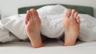 Kadın yalınayak, yakın plan çekimde, yan yana sallanıyor, yatakta yatıyor. Kuru tabanlar. Tatil ve dinlenme kavramı.