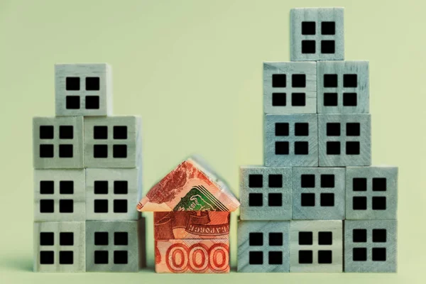 Demolition of buildings. A small origami house made of Russian rubles next to high-rise buildings made of cubes. The concept of a loan, mortgage and porchase of real estate.