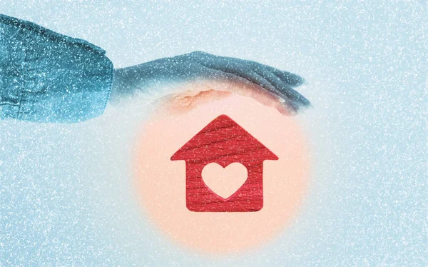 Heating of houses. A woman\'s hand protects a red little house with a heart in a warm round glow. Blue background with snow. The concept of insurance and property protection.