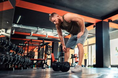 Genç sakallı atletik bir adam spor salonunda dambıllarıyla antrenman yapıyor. Alt manzara. Zindelik ve sağlıklı yaşam tarzı kavramı.