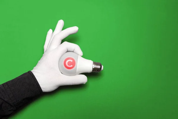 International Intellectual Property Day. A white-gloved hand holds a light bulb with an intellectual property symbol. Copy space. Green background. The concept of copyright and ideas.