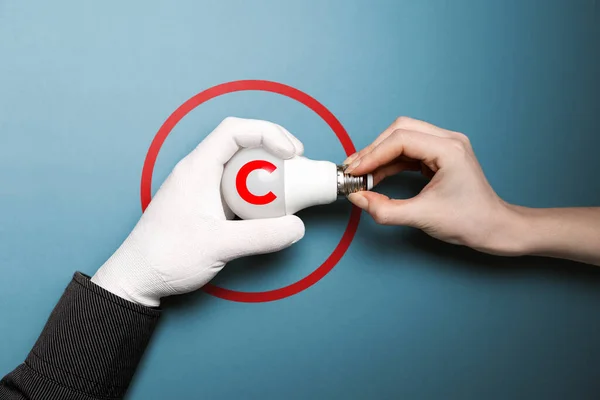 International Intellectual Property Day. A white-gloved hand takes the light bulb with the intellectual property symbol from the other hand. Blue background. The concept of copyright and ideas.