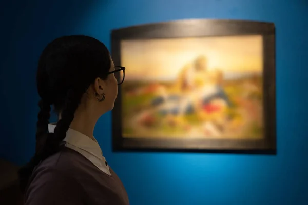 History and culture. Back view of young Caucasian woman in museum contemplates arts and pictures. Visiting excursion in exhibition. Concept of historic education.