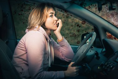 Traffic accident. A scared young blonde nervous woman is sitting behind the wheel of a left-hand drive car and bites her nails. Side view. Blood on the windshield of the car.