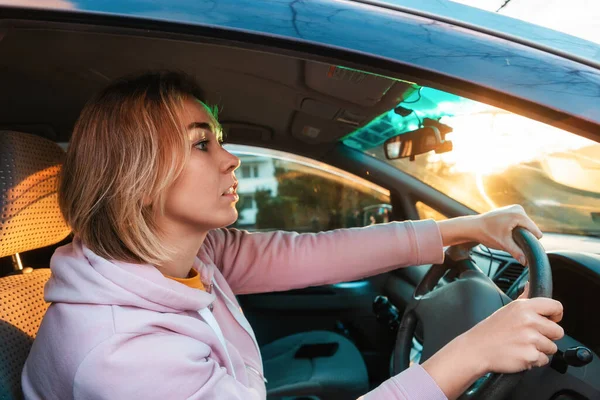 Portrait of young caucasian woman is sitting at the wheel of a right-handed car and anxiously looks at the road. Traffic rules concept.