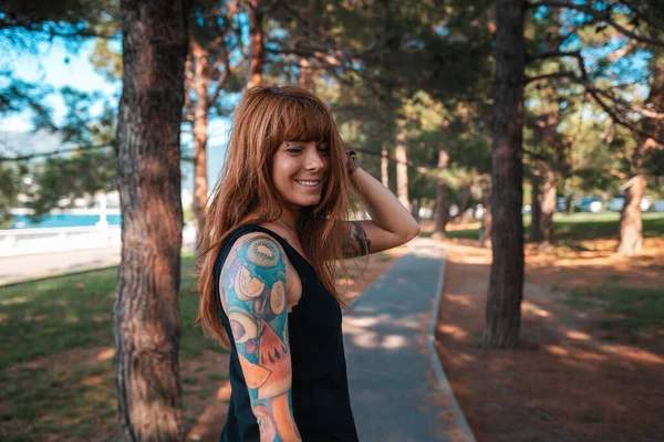 Portrait of a young happy woman with a tattoo on her arm is walking in the park. Summertime.