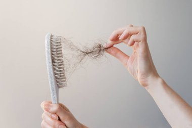 Female hand pulls out a clump of hair from a comb. Close-up. The concept of alopecia and hair loss.