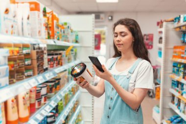 Shopping. Young pretty woman taking photo of a jar of cream in a cosmetics store.