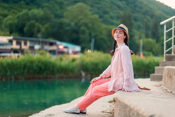 一个穿着夏装 头戴草帽的年轻貌美的快乐女人坐在码头旁 暑假和放松 — 图库照片