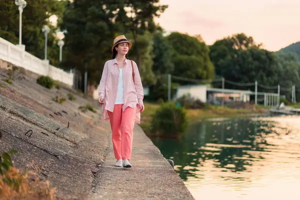 一个穿着夏装 头戴草帽的年轻时髦女人走在河边 — 图库照片