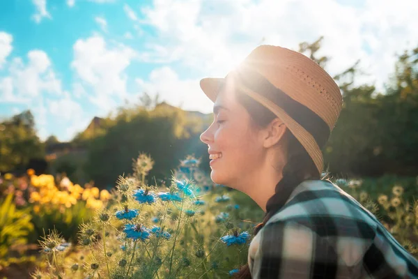 一个戴着草帽的年轻快乐女人的画像 闻到了黑色花的芬芳 侧视图 — 图库照片