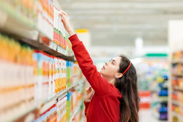 Young Caucasian Woman Red Sweater Reaches Juice Box Top Shelf — Stockfoto