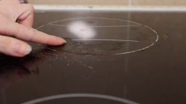 Woman's hand scrapes induction hob with finger. Dry dirty and stove close up. Concept of chores and cleaning service.
