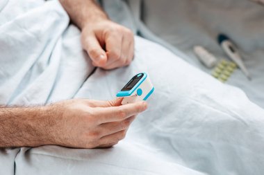 Patient lying at bed and check the data at pulse oximeter. Close up of hands. Concept of determination of oxygen in the blood.