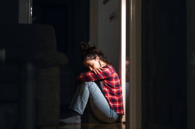 Depresyon ve zihinsel bozukluk. Kafkasyalı genç bir kadın, karanlık odada çaresizlik ve ıstırap içinde yerde oturuyor. Yan görüş. Psikolojik sağlık kavramı.
