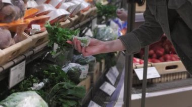 Kadın süpermarkette organik maydanoz seçiyor. Hipermarkette doğal taze tarım ürünleri. Sebzeli el ve raflara yakın çekim.