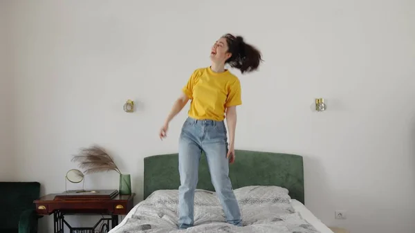 ジーンズと黄色のシャツを着たベッドの上で幸せな若い白人女性面白いダンス 自由と休日の概念 — ストック写真