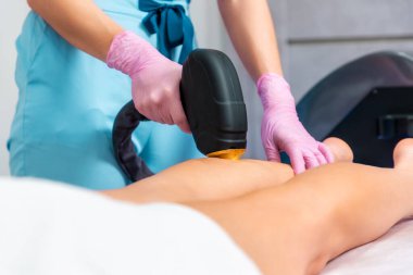 Kozmetik uzmanı kadının bacağında lazer tüy çıkarma prosedürü uygular. Ayakları kapatın. Güzellik salonunda epilasyon ve profesyonel bakım konsepti.