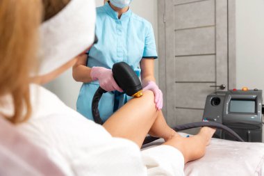 Professional cosmetologist does a laser hair removal procedure on knee at woman. The concept of epilation in beauty salon.