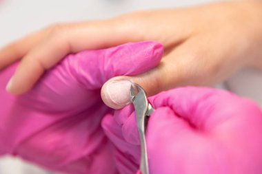 A master in medical pink gloves cuts off the cuticle with clippers. Close-up. The concept of manicure and salon nail care.
