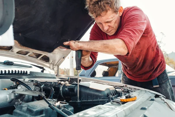 The concept of disability of people and their adaptation to life. A blond disabled man repairs a car, works with a screwdriver. There are no fingers on his hands.
