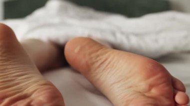 Bacakları battaniyenin altından sarkıyor. Çıplak ayaklı, nasırlı ve nasırlı bir kadın. Odaklanmamış görüntüyü büyüt.