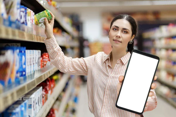 超市的销售 年轻白种人美女的肖像展示了白色屏幕的大型智能手机 并模仿和从货架上取货 折扣应用的概念 — 图库照片