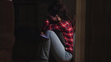 Depresyon ve zihinsel bozukluk. Genç, ağlayan beyaz kadın yerde çaresizce oturuyor ve cep telefonu kullanıyor. Yan görüş. Psikolojik sağlık ve üzüntü kavramı.
