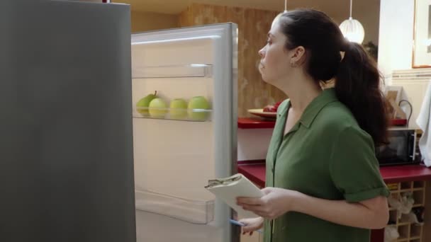 Boční Pohled Mladé Kavkazské Ženy Otevřené Ledničky Píše Seznam Produktů — Stock video