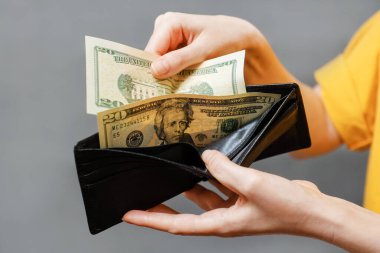 Tasarruf. Bir kadının elleri siyah deri bir cüzdandan dolarları çıkarır. Yakın plan. Alışveriş ve ödeme kavramı.