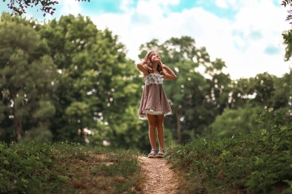 幸せな子供時代 藁帽子に身を包んだ可愛い女子高生が坂の上に立って見上げます 公園と空を背景に 学校の休日 自由と夏の概念 — ストック写真