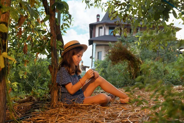 独自一个戴着草帽的漂亮的高加索小女孩坐在花园里的地上 地方耕作的概念和心理 — 图库照片