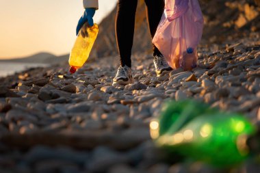 Atık geri dönüşümü ve sosyal sorunlar. Bir gönüllü çakıl taşı plajı boyunca yürür ve çöp torbasında plastik şişe toplar. Düşük açı. Kıyı bölgelerini kirlilikten temizleme kavramı.