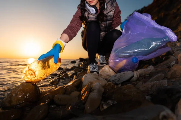 A female volunteer picks up garbage on the ocean. Cleaning of the coastal zone and preservation of ecology. Trash collection for recycling. Concept of Earth Day.