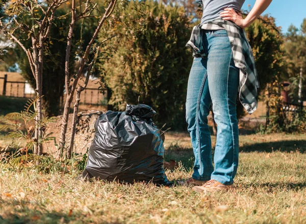 The concept of environmental pollution and Earth day. A woman volunteer removes garbage in the Park, near the feet is a black garbage bag. Close up. Tint.