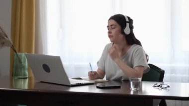 Kulaklık takan genç beyaz kadın sıkıldı ve dizüstü bilgisayarda çalışıyor. Merkez ofis. Serbest ve uzak çalışma.