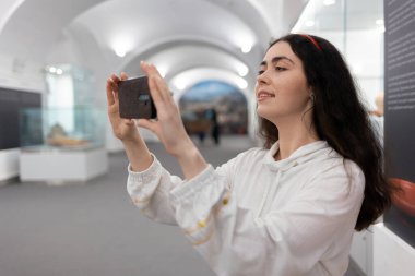 Kafkasyalı genç bir kadının müze gezisinde akıllı telefon kullanışının yan görüntüsü. Modern uygulama eğitimi.