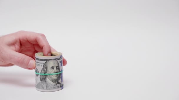 お金の節約 男の手はドルのロールアップバンドルを示しており 女性の手の横に小さな貯金箱を置きます 白い背景に手を閉じてください 株式市場 資金の蓄積の概念 — ストック動画