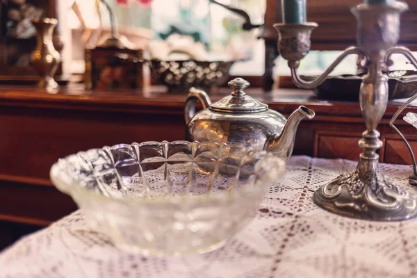 Vintage furniture and glassware on table with napkin. Silver teapot and candlestick. Retro interior of coffee shop.