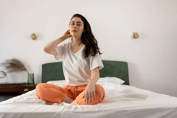 Stock image Young Caucasian woman sitting cross-legged on bed in bedroom. Concept of yoga and wellness.