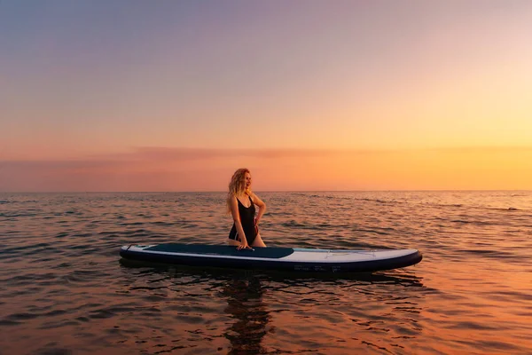 海の中でアップボードでポーズをとる白人の美しい若い女性 コピースペース 背景には金色の夕日 海でのスポーツレクリエーションの概念 — ストック写真