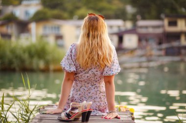 Yalnız sarışın kadın nehir kenarında oturuyor, arka manzaralı. Yaz tatili, özgürlük ve psikoloji kavramı.