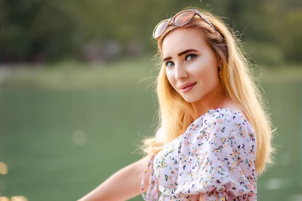 stock image Portrait of a beautiful young blond woman against the background of a river. The concept of summer vacation, freedom and psychology.